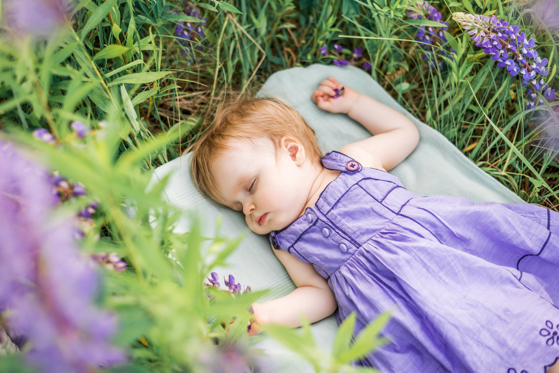 Photo of a sleeping baby girl on a blanket in the grass surrounded by plants showing how green noise with nature sounds calms babies helping them to sleep deeply