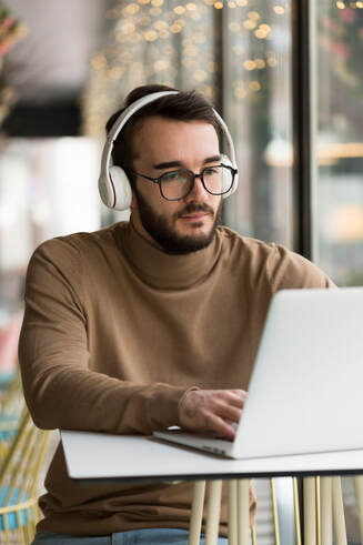 PPerson working at a laptop with headphones listening to ambient music, bathed in soft light, focused on a creative project