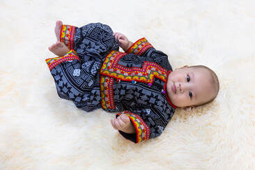 Photo of beautiful asian baby with bright clothing from tibet, nepal, china, or japan listening to calming lullabies from around the world 