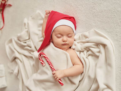 Peacefully sleeping baby listening to Christmas lullabies with a santa hat on while holding a candy cane.