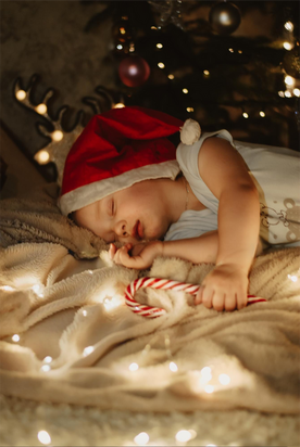 Soft glowing Christmas lights around a peaceful sleeping baby with a candy cane and santa hat, representing gentle instrumental holiday lullabies that help babies relax and fall asleep.