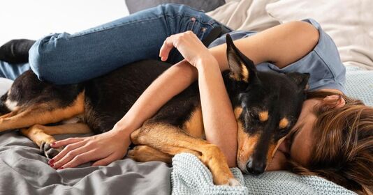 Woman and dog relaxing and sleeping on a bed while listening to nature sounds, white noise, and ambient music from the sleep and relaxation blog to calm them