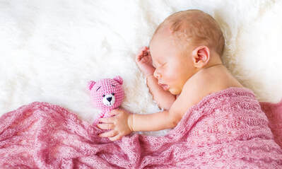 Newborn baby sleeping peacefully under a pink blanket while holding a pink teddy bear -- calm sleep environment supported by pink noise.
