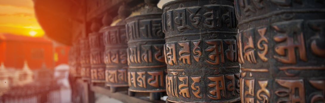Close-up of Buddhist prayer wheels in Tibet with an orange sunset in the background showing peace, relaxation, and healing through music and prayer