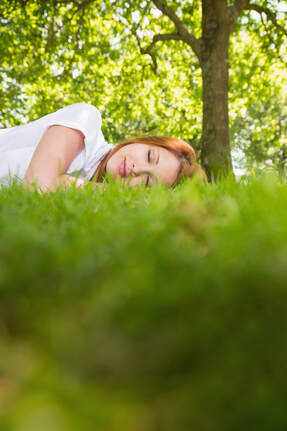 Pretty young red haired woman sleeping peacefully in the green grass outside on a warm summer day to show how green noise and nature sounds promote deep sleep
